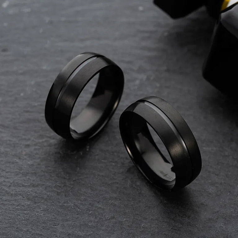 Two minimalist Matte Black Rings showcased against a contrasting dark, grainy backdrop.