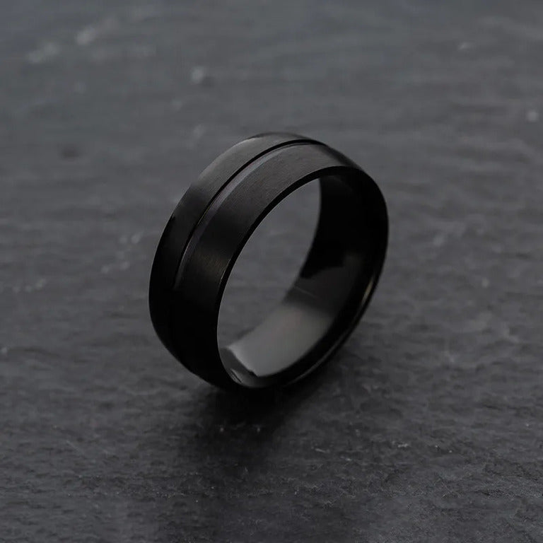 Minimalist Matte Black Ring showcased against a contrasting dark, grainy backdrop.