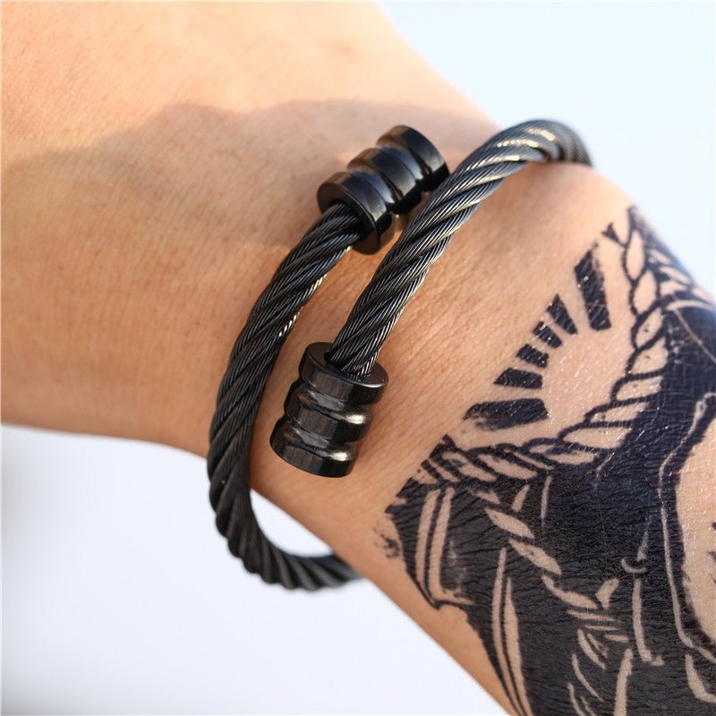 Close-up of a model's wrist showcasing a unique, retro-inspired black titanium steel winding bracelet, contrasted against a graphic black tattoo.