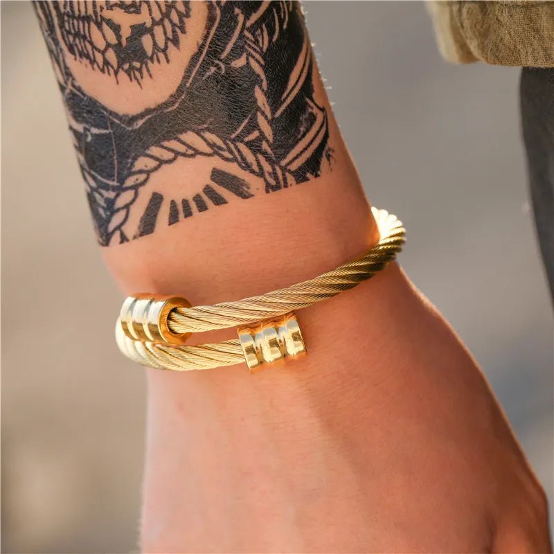 Close-up of a model's wrist showcasing a unique, retro-inspired gold titanium steel winding bracelet, contrasted against a graphic black tattoo.