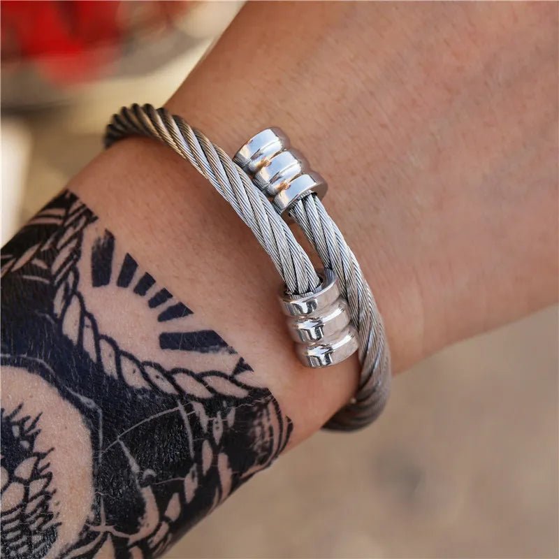 Close-up of a model's wrist showcasing a unique, retro-inspired silver titanium steel winding bracelet, contrasted against a graphic black tattoo.